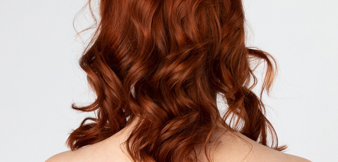 Frau mit langen, roten, welligen Haaren steht mit dem Rücken zur Kamera.